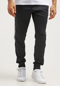 Svarta träningbyxor av mjukt tyg, med vita sidosträck, smal passform och en broderad logga på vänster ben.