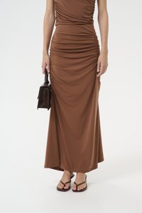 Brown, form-fitting maxi dress with side ruching detail. Paired with dark brown handbag and brown flip-flops. Smooth fabric texture.