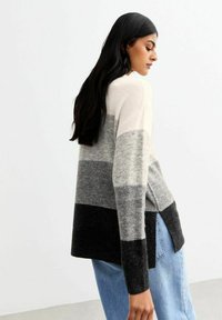 Pull en tricot avec un design coloré en gris clair, gris foncé et noir, offrant une coupe ample et des fentes sur les côtés, fabriqué en tissu doux.