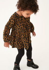 Leopardmönstrad klänning i brunt och svart tyg med volanglager, långa puffiga ärmar, kombinerad med svarta leggings och glänsande svarta stövlar.