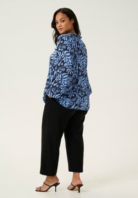 Langärmlige Bluse in Blau und Marine mit floralem Muster, kombiniert mit schwarzen eng anliegenden Hosen und schwarzen Riemchenabsätzen. Weicher, fließender Stoff.