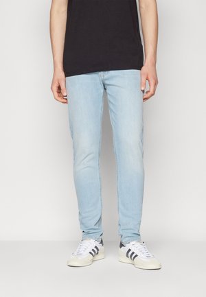 Jeans de mezclilla azul claro con un corte ajustado y un ligero desgaste. Combinados con zapatillas blancas que tienen franjas negras.