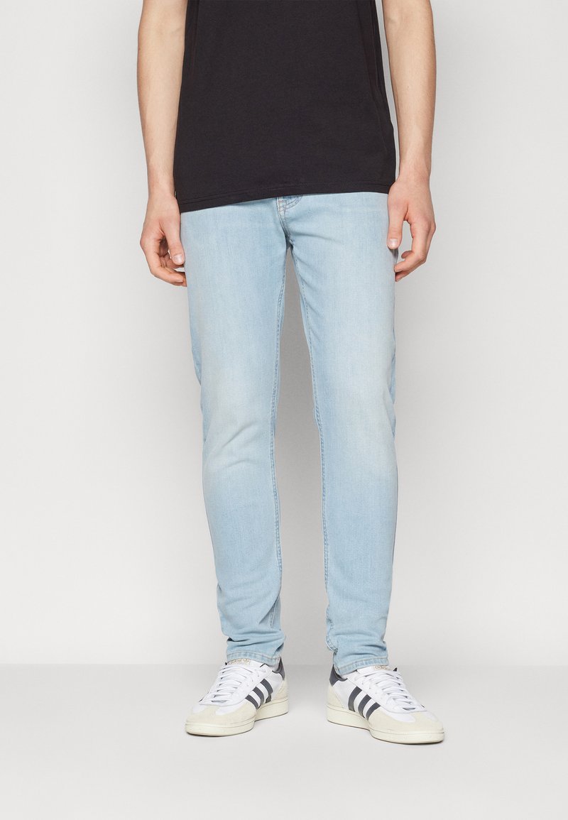 Jeans de mezclilla azul claro con un corte ajustado y un ligero desgaste. Combinados con zapatillas blancas que tienen franjas negras.