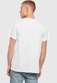 Baltos medvilnės marškinėliai trumpomis rankovėmis ir apvaliu iškirpimu, turintys paprastą dizainą ir lygų paviršių. Rodoma nugarinė pusė.