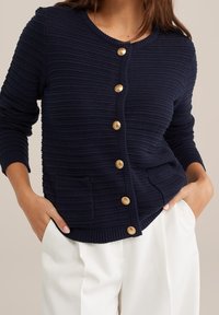 Námořnický pletený kardigan s texturovaným povrchem, kulatým výstřihem, šesti zlatými knoflíky a dvěma předními kapsami.