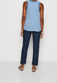 Top senza maniche a righe blu e bianche, abbinato a jeans dritti blu scuro e sandali silver a scivolo, visto da dietro.