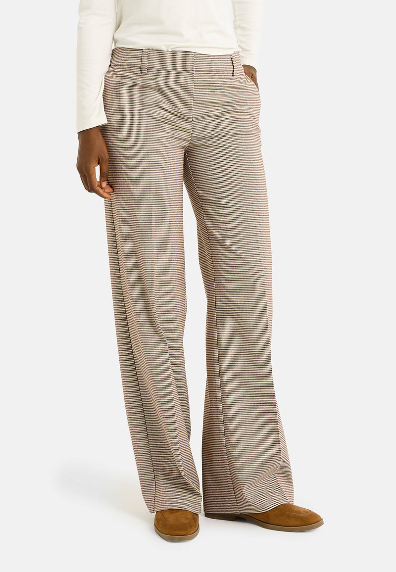 Pantalones de pierna ancha a cuadros marrones, confeccionados con una tela suave. Cuentan con bolsillos frontales y pasadores para cinturón, complementados con un calzado casual.