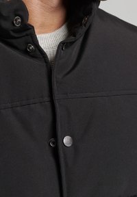 Svart jacka med tryckknappslås och hög krage, med en mjuk textur och minimalistiska design detaljer.