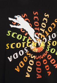 Camisa negra con un diseño gráfico dinámico que presenta un animal saltando en blanco y las palabras "SCOTCH SODA" en múltiples colores, irradiando hacia afuera.