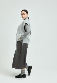 Graues ärmelloses Oberteil mit Seitentaschen, kombiniert mit einem langen schwarzen Lederrock. Graue Socken und schwarze Schuhe runden das Outfit ab.