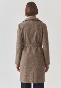 Bruine gewatteerde wollen jas met een ceintuur in de taille, notch kraag en een ventilerende achterkant. Eenvoudig ontwerp met een middellange snit, geschikt voor het dragen in lagen.