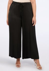 Černé kalhoty s širokými nohavicemi a volným střihem, elastický pas a šňůrka. Hladká, lehká tkanina bez viditelných vzorů nebo akcentů.