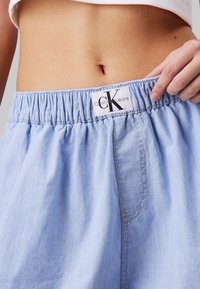 Pantalones cortos ligeros de color azul claro con cinturilla elástica y un bolsillo lateral, con una etiqueta que dice "Calvin Klein Jeans."