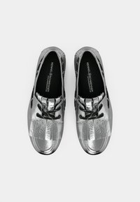Μεταλλικά ασημένια παπούτσια με στρογγυλεμένη μύτη, σχέδιο με κορδόνια και πιετέ λεπτομέρειες στο πάνω μέρος. Υφή επιφάνειας με λαστιχένια σόλα.