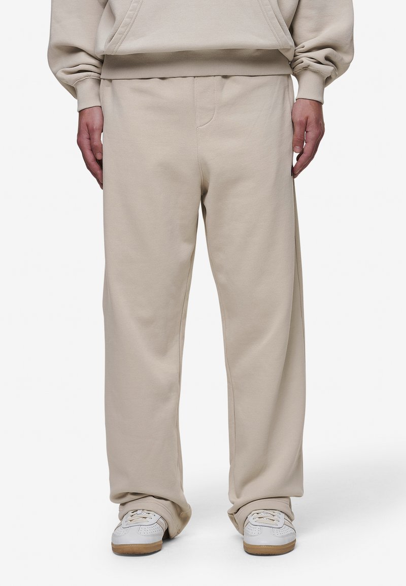 Beige sweatpants made of soft fabric, featuring a relaxed fit, elastic waist, and visible stitching detail on the front.
