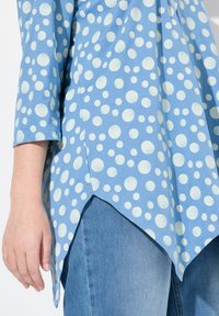 Blauwe tuniek met witte stippen, voorzien van driekwartmouwen en een high-low zoomontwerp, gecombineerd met denim. Glad textuur.