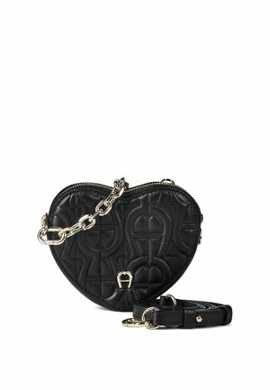 Sac en cuir noir matelassé en forme de cœur avec poignée chaîne dorée et bandoulière en cuir noire amovible sur fond blanc.