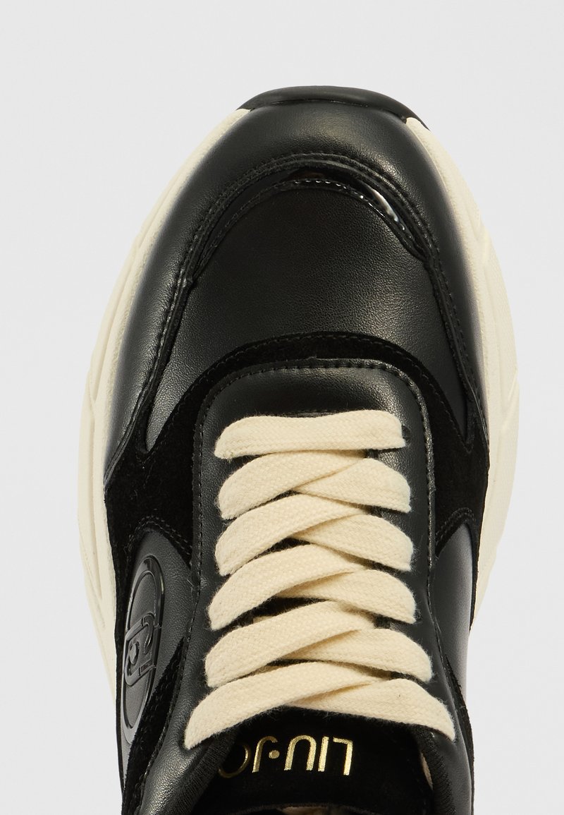 Schwarze Sneaker mit einem glatten Obermaterial aus Leder und Wildlederakzenten. Cremfarbene Schnürsenkel, strukturierte Außensohle und ein Logodetail in der Nähe der Ferse.