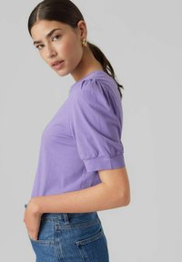 Lavandos spalvos trumpomis rankovėmis palaidinė su pūstomis petnešomis, minkštas medvilninis audinys ir apvalus iškirpimas. Dėvima su aukštu liemeniu mėlynomis džinsinėmis kelnėmis.