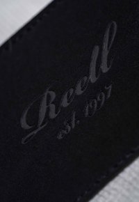 Black leather wallet featuring embossed text "Reell est. 1997". Smooth texture with subtle stitching detail along the edges.