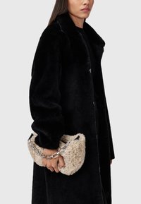 Čierny kabát z umelej kožušiny so širokým golierom a zapínaním na gombíky, doplnený béžovou plyšovou kabelkou so strieborným reťazovým popruhom.