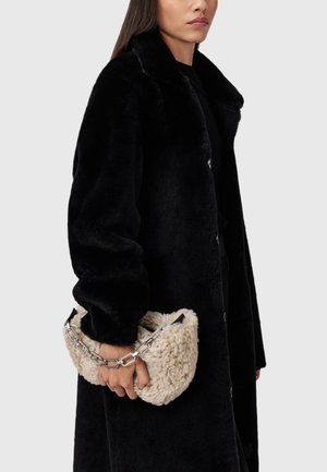 Crni kaput od umjetnog krzna s širokim ovratnikom i zatvaranjem na gumbe, u kombinaciji s bež pahuljastom torbom za ruku sa srebrnim lancem kao remenom.