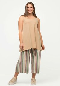 Top senza maniche beige con vestibilità rilassata, abbinato a culotte a righe chiare con accenti verdi, rosa e blu. Sneakers beige semplici.