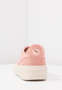 Baskets Puma en daim rose avec une épaisse semelle blanche et un logo Puma doré à l'arrière, photographiées sur fond blanc.