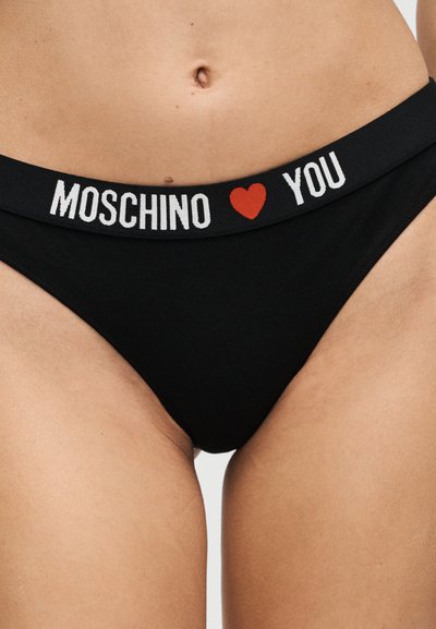 Μαύρα εσώρουχα με ελαστική ζώνη μέσης που φέρει τα λόγια "MOSCHINO" και "YOU" χωρισμένα με μια κόκκινη καρδιά, φορεμένα στο κάτω μέρος της κοιλιάς και τους γοφούς ενός ατόμου.