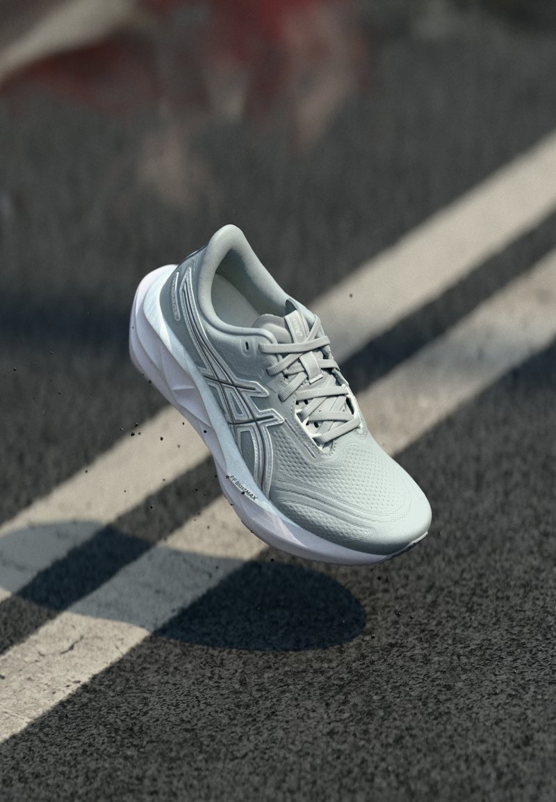 Ανοιχτό γκρι αθλητικό παπούτσι με λευκή σόλα στον αέρα πάνω από άσφαλτο δρόμο με λευκές διαγραμμίσεις.