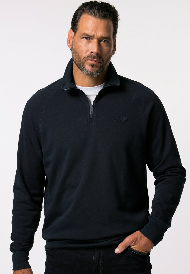 Sudadera de media cremallera en azul oscuro, fabricada en un tejido suave. Presenta un cuello y puños de canalé, con un sutil logo bordado en el pecho.