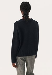 Dunkelblauer Pullover mit strukturiertem Finish, weitem geripptem Saum und überschnittenen Schultern, kombiniert mit grauen karierten Hosen. Einfaches Design.