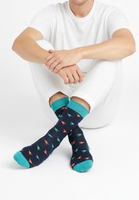 Temno modre nogavice z barvnimi vzorci ptic, turkiznimi manšetami in prsti. Mehka tkanina z gladko teksturo. Oblečene na sedi osebi.