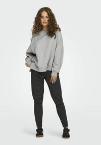 Šedá oversized mikina se širokými rukávy, spárovaná s užšími černými kalhotami se strukturovaným vzorem a tmavými teniskami.