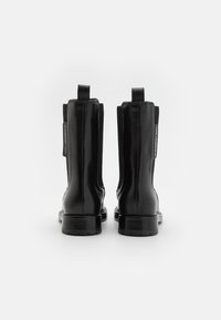 Black leather ankle boots with a smooth finish, elastic side panels, and pull tabs, featuring a solid rubber sole and minimalistic design.