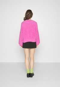 Luddig rosa tröja med långa ärmar, kombinerad med en svart kjol. Funktioner inkluderar en grov textur och en avslappnad passform; bärs med gröna strumpor och svarta skor.