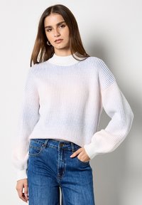 Lichte, ribbelgebreide trui in een gradatie van wit met subtiele blauwe tinten; heeft lange, licht gepofte mouwen en een hoge hals. Draagt u met spijkerbroeken.