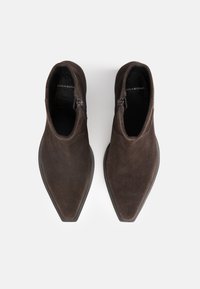 Brown suede ankle boots with a pointed toe and side zipper. The sole is flat and slightly textured, offering a sleek, modern design.