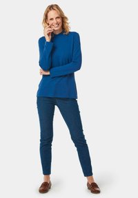 Blaues Langarmoberteil mit hohem Kragen, kombiniert mit dunkelblauen Slim-Fit-Jeans und braunen Slippern. Weicher Stoff, lässiges Design.