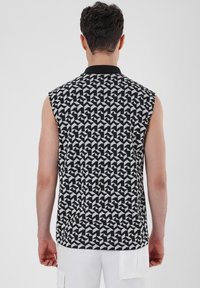 Black and white sleeveless shirt featuring a geometric pattern with sharp angles, round collar, and a textured fabric.