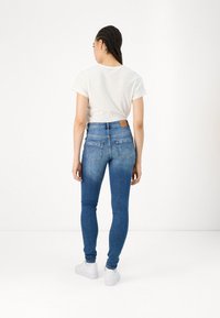 Zilā skinny džinsos ar augstu jostasvietu, ar aizmugurējām kabatām, vieglu izbalēšanu un ādas uzliku pie jostasvietas, kombinēti ar baltu T-kreklu.