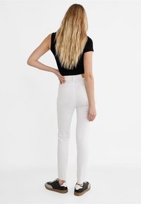 Vita tajta jeans med bakfickor, hög midja, i kombination med svartvita sneakers, sedd bakifrån.