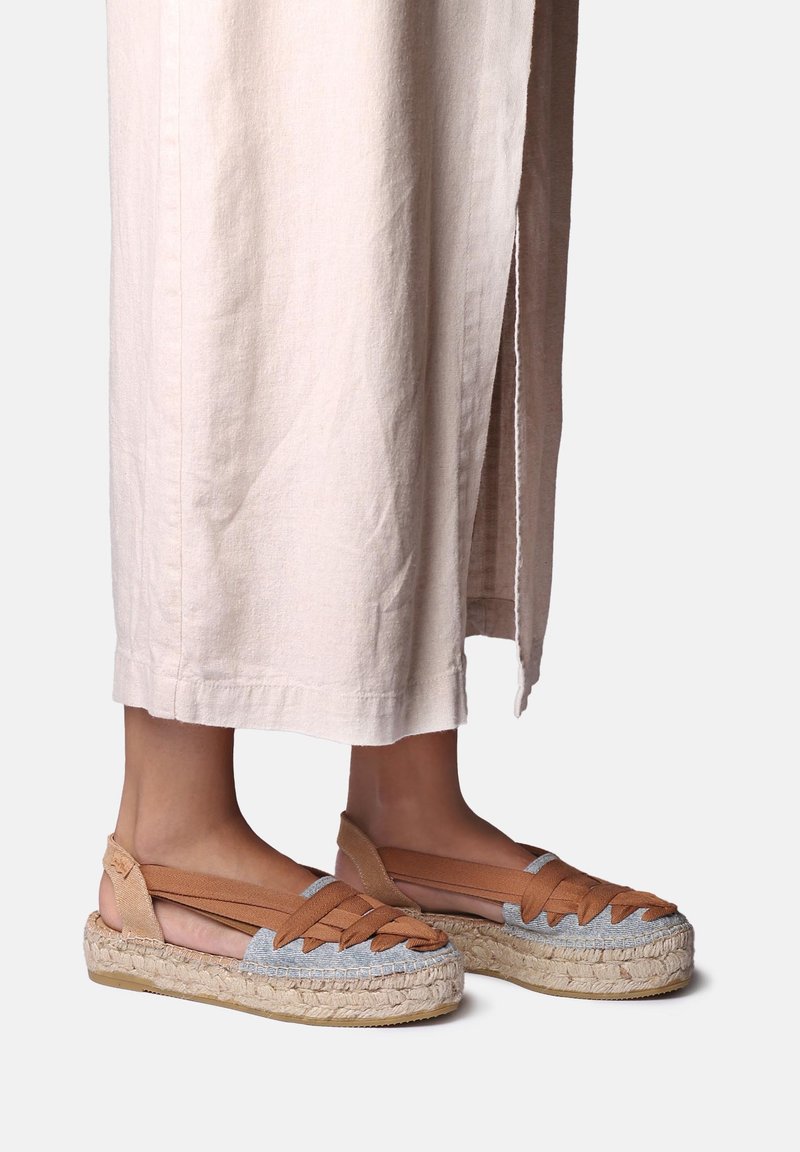 Brown and blue espadrilles with woven straps and a natural jute sole. The shoe has an open back design and a flat heel.