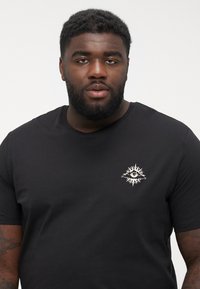 Black cotton t-shirt featuring a small, embroidered sun and eye design on the chest; short sleeves and a classic crew neckline.
