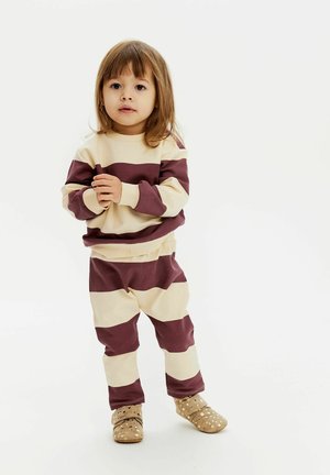 Tuta a righe per bambini in crema e bordeaux; tessuto morbido, maniche lunghe, vita elastica, abbinata a pantofole a pois.