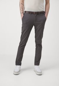 Chino-Hosen aus einem dunkelgrauen Baumwollmischgewebe, Slim Fit mit flacher Vorderseite und seitlichen Taschen, kombiniert mit einem braunen Gürtel und weißen Sneakers.