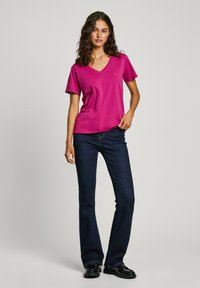 Camiseta de algodón fucsia con escote en V y mangas cortas, combinada con jeans acampanados de un azul oscuro, con una textura suave y un mínimo de detalles.