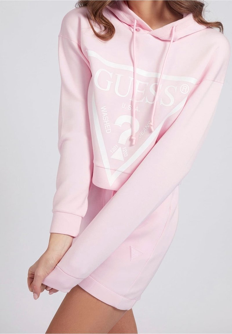 Hoodie court rose clair avec logo blanc et détails graphiques, doté d'une capuche à cordon de serrage et de poignets côtelés. Texture de tissu lisse.