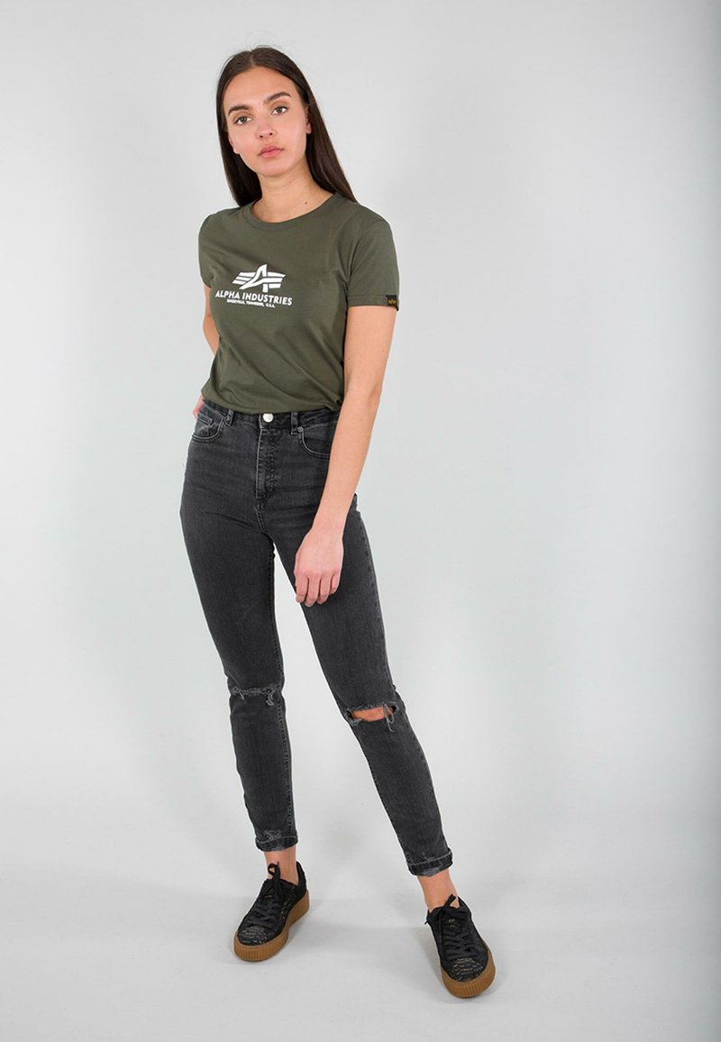 Olivgrön t-shirt med kort ärm och vitt logo, högmidjade svarta jeans med slitna knän, och svarta sneakers med texturerade detaljer.