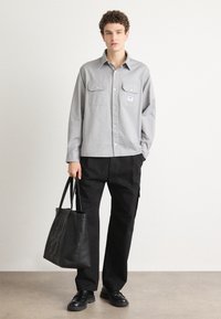 Light gray button-up shirt with two chest pockets, paired with black pants and a black tote bag. Smooth texture and relaxed fit.